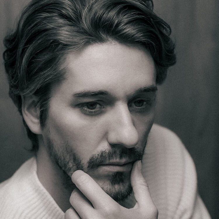 Studio portrait of young photographer in white sweater with thoughtful expression and hand near chin