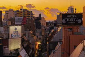 Tokyo Cityscape at Sunset A vibrant cityscape of Tokyo at sunset, featuring illuminated hotel signs and a dramatic sky with scattered clouds.