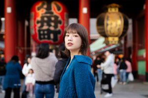 Young woman in a blue sweater posing in front of a traditional Japanese temple gate, capturing the essence of Tokyo's cultural heritage.