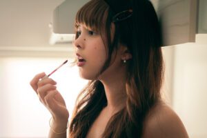 Editorial beauty close-up: female model applies bold red lipstick in dramatic cinematic lighting in a Tokyo photo studio, perfect for makeup brands or fashion campaigns.