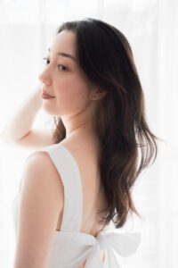 A model poses gracefully in a white dress against a soft, neutral backdrop in a studio in Tokyo. The image captures her natural elegance and poise, perfect for fashion and commercial portfolios.
