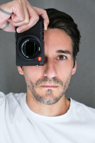 JG Studio photographer, holding a Leica camera up to his eye, showcasing his involvement in photography.