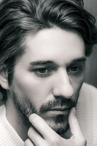 A black and white portrait of JG Studio owner, posing thoughtfully with his hand resting on his face.