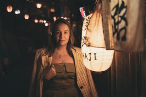 Elegant woman in a stylish outfit standing under a warmly lit paper lantern, highlighting fashion photography in Tokyo.