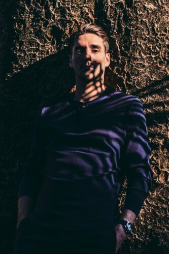 JG, a versatile fashion model in Tokyo, posing in a dark long-sleeve shirt against a tree.