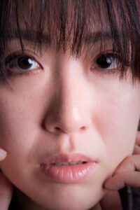 A close-up portrait of a person with striking eyes and neatly combed hair, resting their chin on their hand, conveying a sense of contemplation and depth.