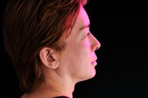 A side profile portrait of a person with pink highlights in their hair, illuminated against a dark background, showcasing a serene and calm expression.