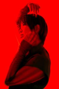 A dramatic portrait of a person with expressive eyes and styled hair, illuminated by striking red lighting, creating a bold and intense visual effect.