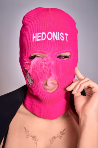 Portrait for the Japanese Brand Hedonist Stylish portrait of a model wearing a vibrant pink balaclava with the word 'HEDONIST' embroidered on it, exuding a bold and playful vibe. The model is captured in a dynamic pose, with smoke adding a dramatic effect, perfect for fashion and lifestyle photography portfolios.