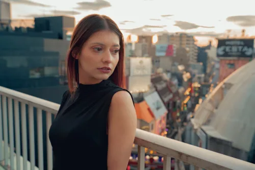 JG Studio Balcony A woman standing on a rooftop with a cityscape in the background during sunset.