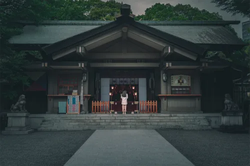 Traditional Japanese photography A woman standing in front of a traditional Japanese shrine, with stone statues on either side of the entrance.