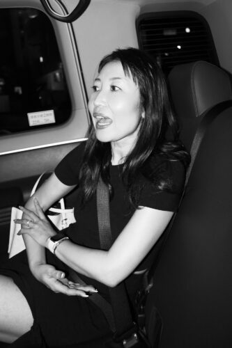 Lifestyle Photography A woman engaged in conversation while seated in a vehicle, wearing a black dress and holding a white handbag.