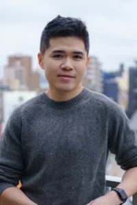 A casual outdoor portrait of a young man wearing a gray sweater, photographed in Tokyo.