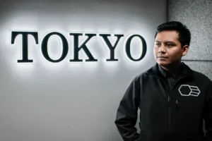 A professional man posing in front of a "TOKYO" illuminated sign, wearing a black jacket, ideal for corporate and portrait photography in Tokyo.