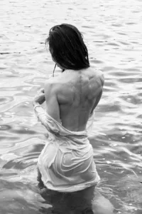 Woman draped in wet fabric sitting in shallow water, evoking serenity and connection with nature.