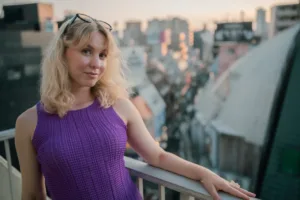 Professional Portrait of Woman on the Studio Balcony A woman in a purple dress leans on a rooftop railing, with the Tokyo cityscape in the background. Lifestyle portrait photography by JG.