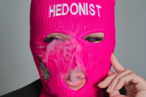 Professional fashion photography for Tokyo streetwear brand Hedonist, with a bold close-up portrait of a female model wearing a vibrant pink balaclava.