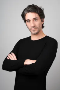 Professional studio portrait of a man with dark hair and a black long-sleeve shirt, posing with arms crossed against a grey background at JG Studio Tokyo.