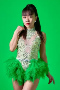 Professional studio portrait of a female performer in a vibrant green sequined and ruffled stage outfit, posed against a bright green screen background in a Tokyo photography studio.