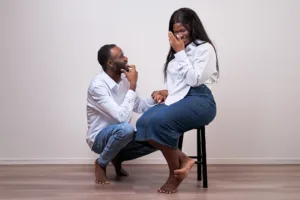 Candid Couple Portrait A man kneeling and smiling at a laughing woman sitting on a stool in a minimalist photography studio in Tokyo.