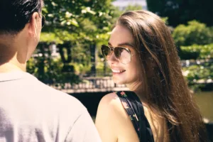 東京の屋外エディトリアル撮影で、アビエーターサングラスを着用し、笑顔で振り返る女性のライフスタイルポートレートのアップ。