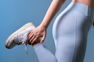 Close-up fitness portrait of a model in pale blue activewear holding a white Nike Air Force 1 against a blue studio backdrop, by JG in Tokyo.