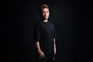 Low-key studio portrait of a man with auburn hair wearing a black t-shirt against a dark background, lit with dramatic side lighting during a portrait session in Tokyo by JG.