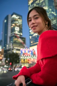 Portrait photography during a Shibuya night tour, model in a red sweater with the illuminated Shibuya Crossing billboards and skyline behind her.