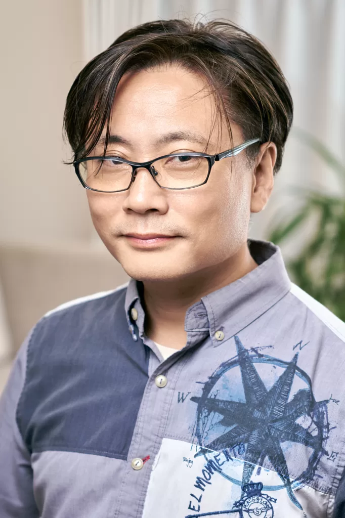Casual business portrait of a man in glasses and a patterned blue shirt, photographed in natural light in a Tokyo office by JG.