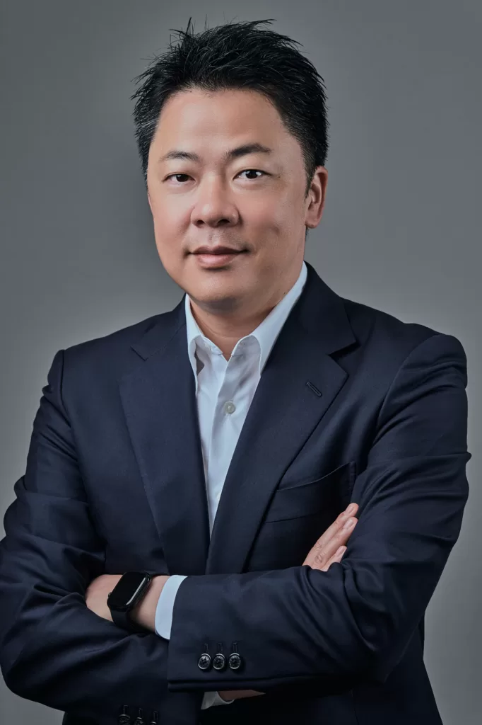 Executive headshot of a man in a navy suit and white shirt with his arms crossed, photographed with studio lighting on a grey background at JG Studio in Shibuya, Tokyo.