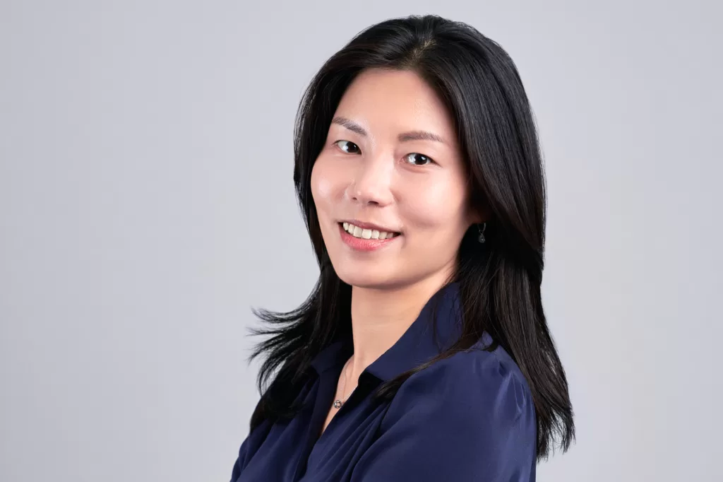 Corporate headshot of a woman in a navy blouse, photographed with studio lighting on a grey background at JG Studio in Shibuya, Tokyo.