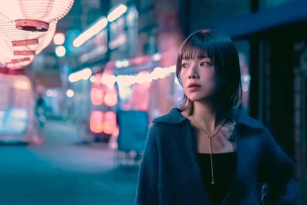 Night portrait of a woman with a short bob under a red paper lantern in Asakusa, teal and pink neon lights blurred behind her.