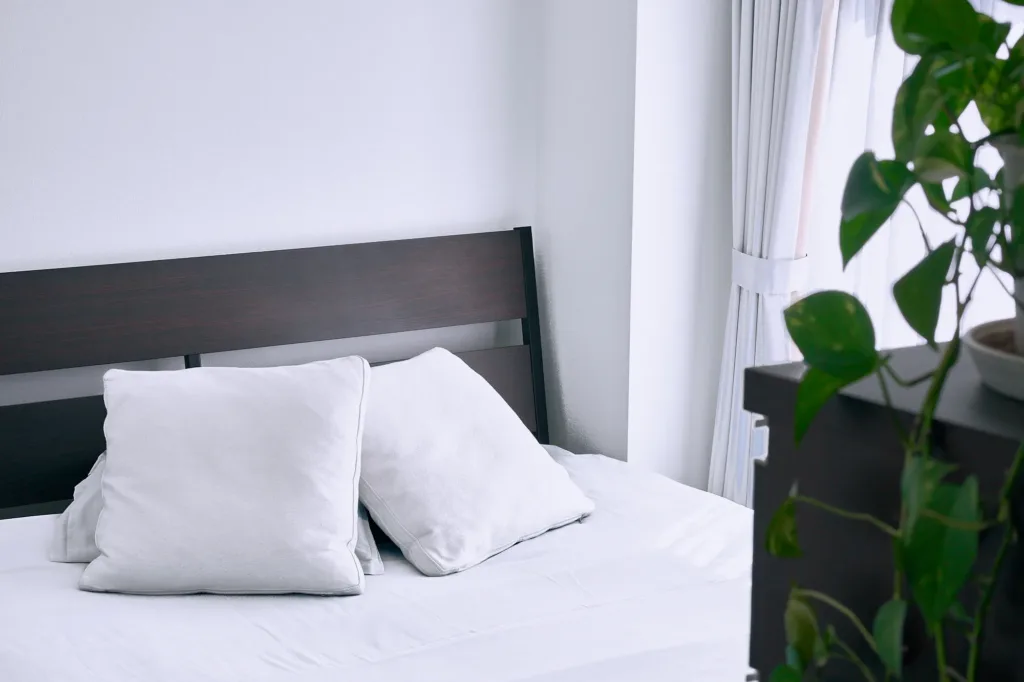 Dark wood bed frame with white bedding and cushions beside a curtained window in the bedroom area of the Shibuya studio.