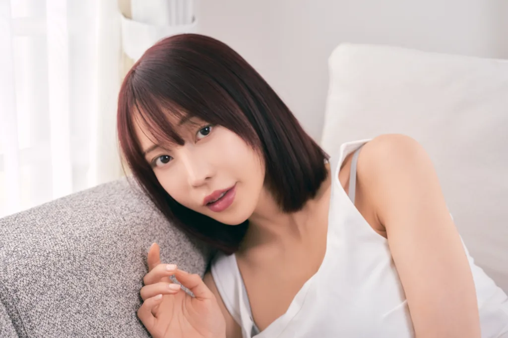 Model in a white tank top reclining on the studio sofa in the soft daylight from the window in Shibuya.