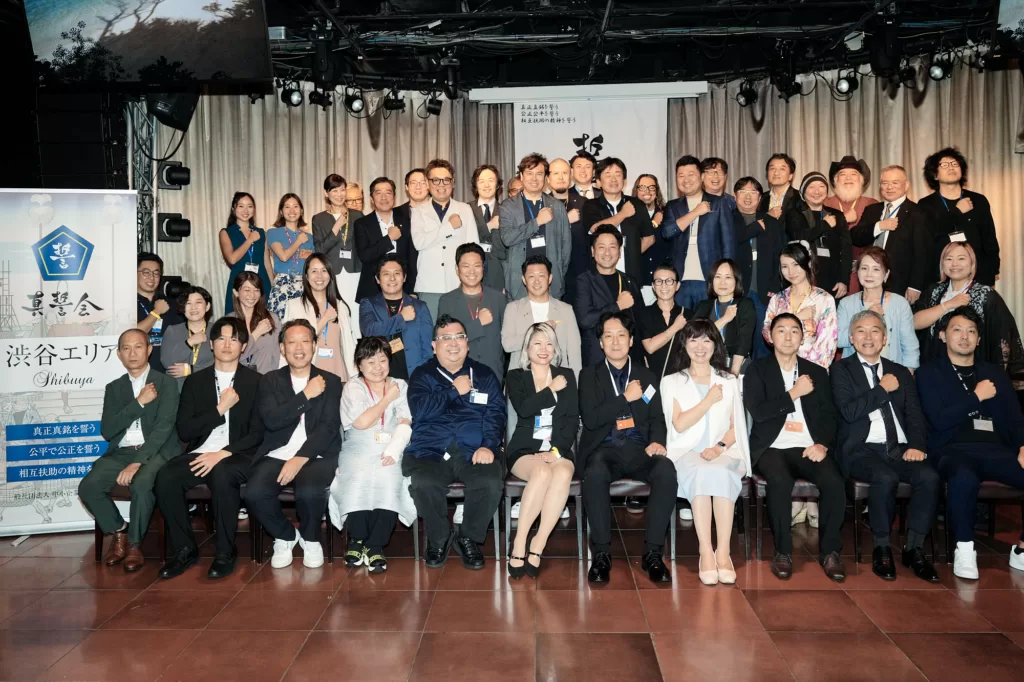 東京・渋谷のビジネス交流イベントで、拳を胸に当てて並ぶ経営者と参加者の集合写真。